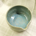Ceramic bowl with blue speckled glaze on a textured beige surface