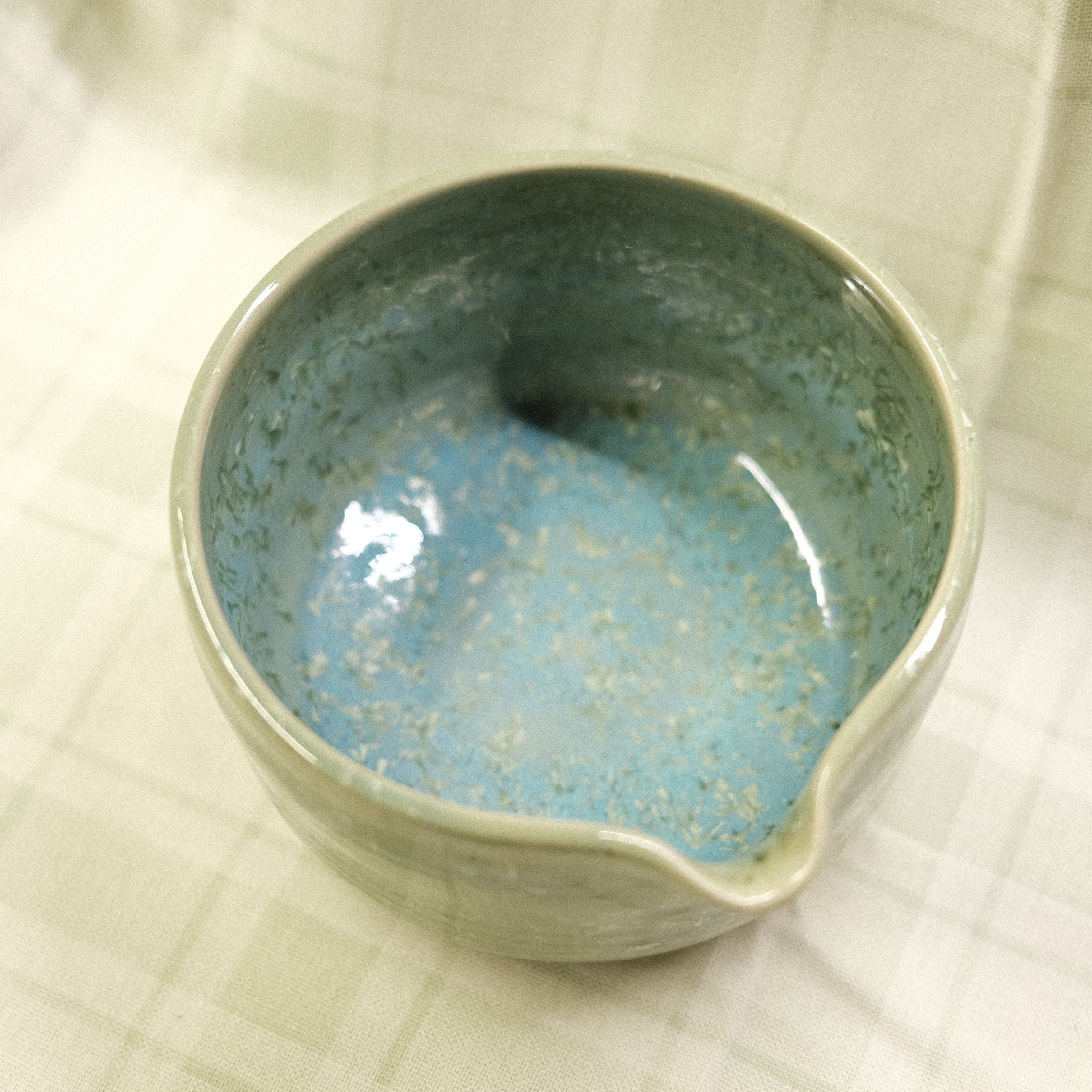 Ceramic bowl with blue speckled glaze on a textured beige surface